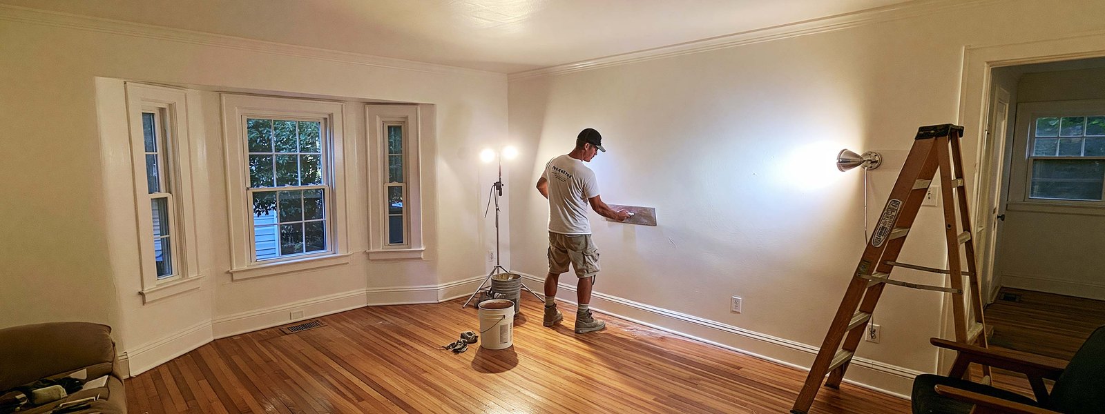 A plasterer skimming a wall in an older house, working under a portable light